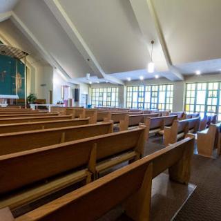 Interior view of a church featuring wooden pews and large windows.
