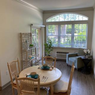 A cozy dining area with a round table, chairs, and abundant natural light from a large window.