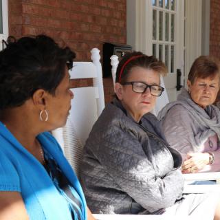 Three people sitting and conversing on a porch during the daytime.