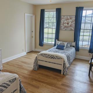 A bright bedroom with twin beds, blue curtains, and wooden flooring.