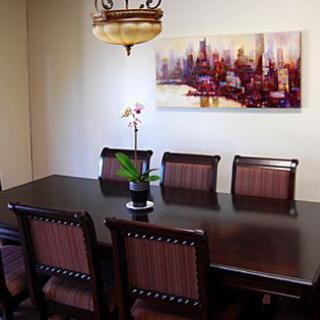 A dining room featuring a dark wooden table with matching chairs, an orchid centerpiece, and cityscape wall art under a chandelier.
