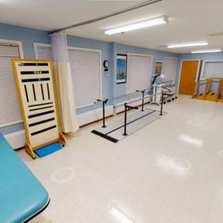 A well-lit rehabilitation room equipped with parallel bars and exercise apparatus for physical therapy sessions.