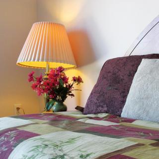 A cozy bedroom setup with a quilted bedspread, decorative pillows, and a lamp illuminating a vase of flowers.