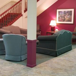 A cozy lobby area with sofas and an armchair arranged around a table lamp beneath a staircase.