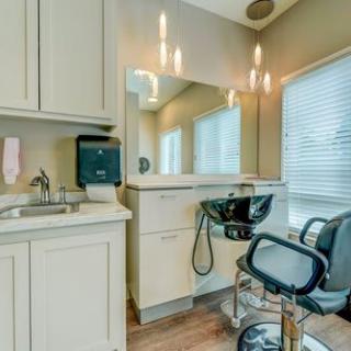 A modern hair salon setup with a styling chair, sink, and well-lit mirror.