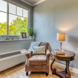 A cozy reading nook featuring a comfortable armchair, side table with a lamp, and a window view.
