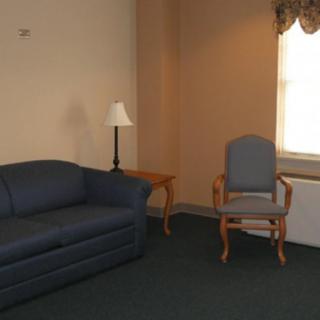 A simple living room with a sofa, chair, and a lamp near a window.