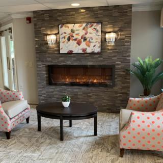 A cozy living room with a modern fireplace, flanked by two patterned chairs and a central wooden table.