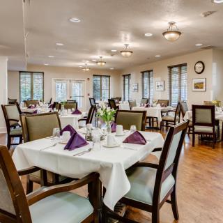 An elegantly set dining room with neatly arranged tables and chairs, featuring soft lighting and tasteful decor.