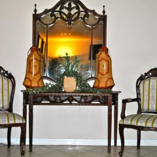 A classic interior setup featuring a carved wooden mirror and matching chairs surrounding a decorative table with ornamental items.