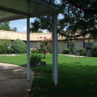 A serene garden area with well-manicured grass and trees, featuring a pathway leading to a building.