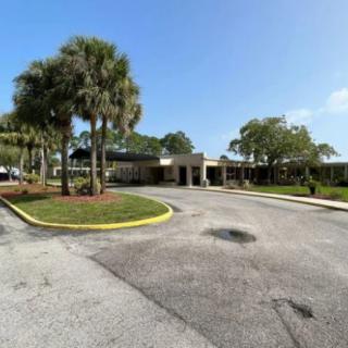 A building with a parking area and palm trees under a clear blue sky.