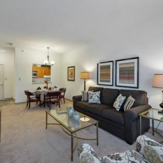 A modern living room with a dining area featuring a sofa, glass coffee table, framed artwork, and decorative lamps.