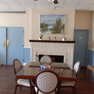 A cozy dining area featuring a table and chairs, with a fireplace decorated with a landscape painting.