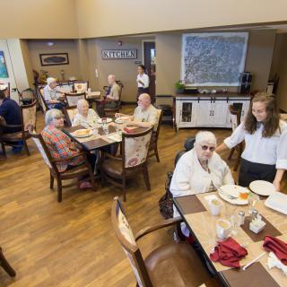 A group of seniors enjoying a meal together in a dining hall at a care facility.