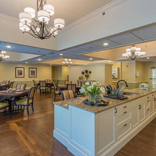 A spacious and elegantly decorated dining area with a central kitchen island, featuring chandeliers and neatly arranged tables and chairs.