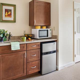 A compact kitchen area with wooden cabinets, a microwave on the counter, and a mini fridge underneath.