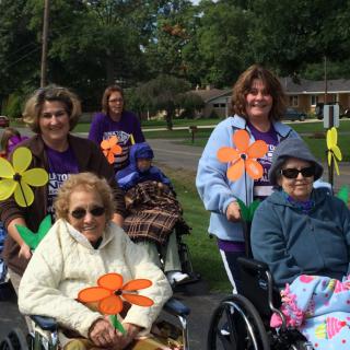 A group of people participating in a parade, holding colorful flower decorations while in wheelchairs.