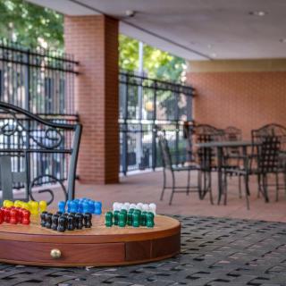 A cozy outdoor patio with colorful jars displayed on a wooden platform, surrounded by chairs and tables under a shaded area with brick walls.