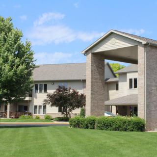 A residential building with a well-maintained lawn and trees under a clear blue sky.