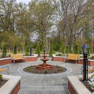 A serene garden with a central fountain surrounded by benches and trees.