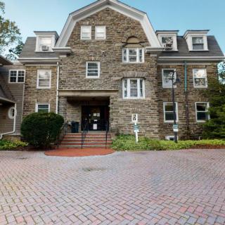 A historic stone building with multiple floors and a welcoming entrance, surrounded by a landscaped area.
