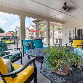 A cozy outdoor patio with colorful cushioned chairs and a table, surrounded by columns and overlooking a scenic view.