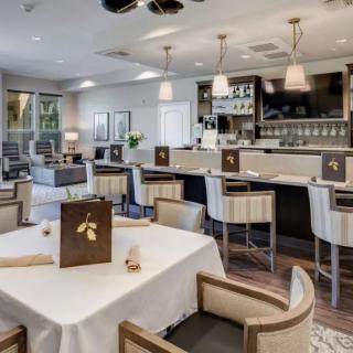 A modern restaurant interior with a dining area featuring elegant tables and chairs, and a well-lit bar.