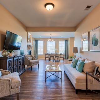 A modern living room with comfortable seating and a view into a dining area, featuring wood flooring and elegant decor.
