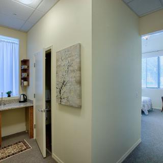 A modern office interior with a minimalist design, featuring artwork on the wall and a small kitchenette area.