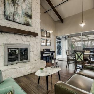A modern living room featuring a stone fireplace, high ceilings with wood beams, and ample natural light.