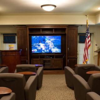 A cozy home theater room featuring comfortable chairs, a large television screen, and a flag in the corner.