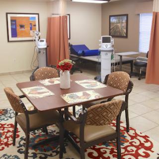 An inviting healthcare space featuring a dining area with chairs, a decorative rug, and patient care stations.