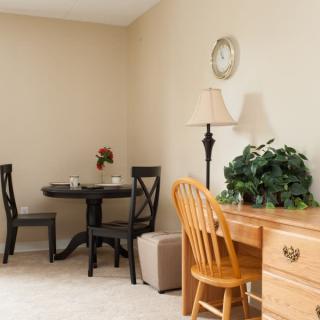 Cozy room corner with a wooden desk, chair, lamp, and small dining table.