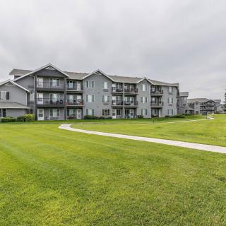 A view of a multi-story apartment building with balconies, surrounded by a well-maintained lawn and an overcast sky.