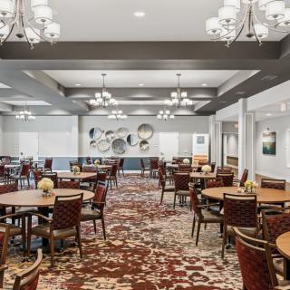 A spacious dining room with elegant chandeliers, neatly arranged tables and chairs, and a richly patterned carpet.