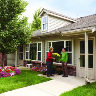 Two people having a conversation outside a house with a garden.