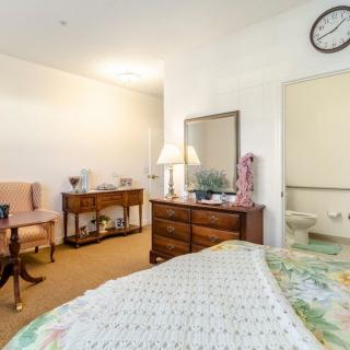 A cozy bedroom with a bed, dresser, mirror, and seating area.