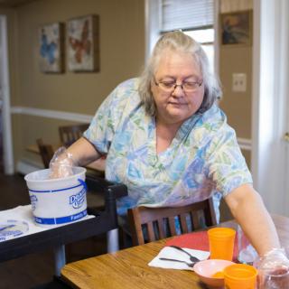 A woman cleaning a kitchen table with cups and a cleaning bucket nearby.