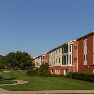 A row of residential apartment buildings with well-maintained lawns and trees under a clear blue sky.