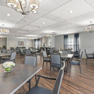 A spacious and elegant dining room with neatly arranged tables and chairs, featuring chandeliers and wooden flooring.
