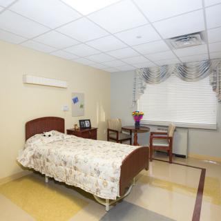 A clean and simple hospital room with a single bed, chairs, and a window with curtains.