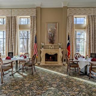 An elegant dining room with large windows, a fireplace, and neatly set tables.