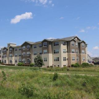 A multi-story apartment building situated in a grassy area under a clear blue sky.