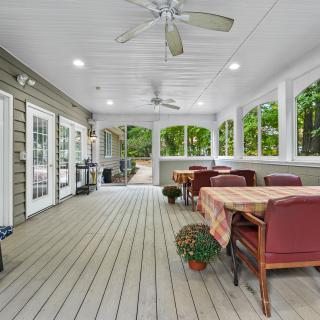 A bright and spacious screened porch featuring comfortable seating, tables with tablecloths, ceiling fans, and potted plants.