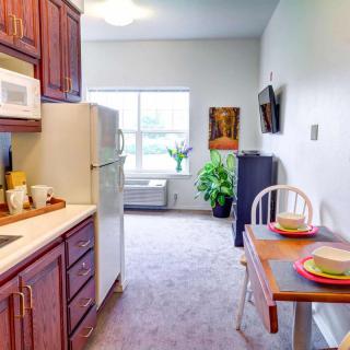 A cozy kitchen and dining area with a table set for two, featuring a refrigerator, microwave, and an indoor plant by the window.