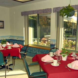 A cozy dining room with neatly set tables, showcasing bright natural light through large windows.