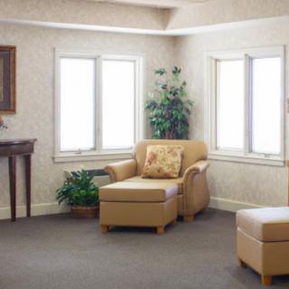 A cozy living room with a comfortable armchair, ottoman, and green plants by the window.