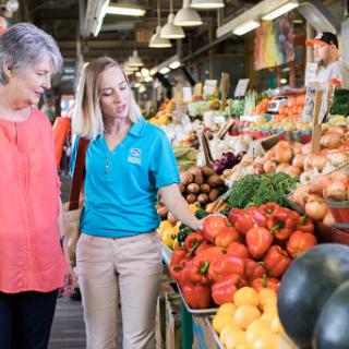 Two women explore the colorful offerings at a vibrant farmers market, discussing fresh vegetables together.