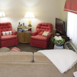 A cozy living room with red armchairs, a sofa, and a television.
